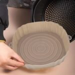 Beige round silicone air fryer liner being placed into an air fryer basket