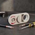 Cable stripping tool on a dark workbench next to coaxial cables, insulating tape and a screwdriver