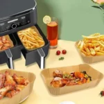 Rectangular paper liners with chicken and fries next to a dual-basket air fryer