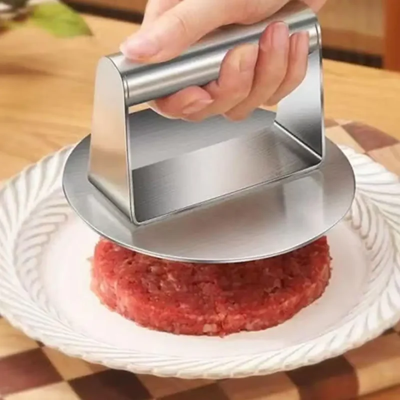 Stainless steel burger press shaping a patty on a plate